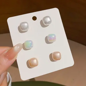 Detail of three pairs of square pearl stud earrings in white, iridescent, and champagne colors.