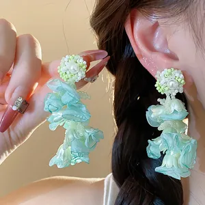 Close-up of light green chiffon flower earrings with pearls and beads in a chic style.