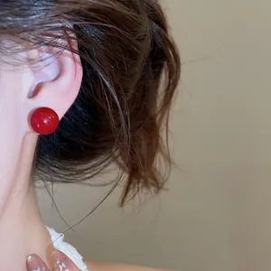 Macro close-up view of an elegant red spherical stud earring worn on the model's ear