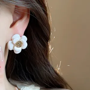 Gros plan détaillé d'une boucle d'oreille fleur en émail blanc avec centre rose doré sur l'oreille