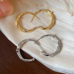 Close-up of elegant gold and silver C-shaped hoop earrings with twisted texture and zircons