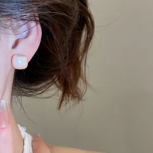 Close-up of a minimalist square pearl stud earring with soft cat's eye glow on ear.