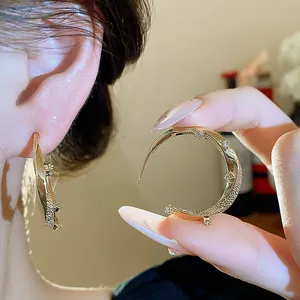 Close-up of elegant gold plated C-shaped earring with sparkling zircon details.