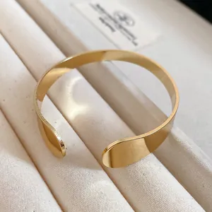 Close-up of a minimalist irregular gold metal open cuff bracelet on a beige jewelry tray