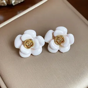 Gros plan d'élégantes boucles d'oreilles camélia en émail blanc avec centre plaqué or 18 carats