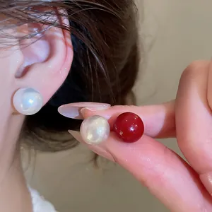 Detailed view of elegant white and red pearl stud earrings worn and held in hand