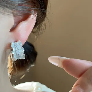 Detailaufnahme von eleganten, silbernen, gefalteten C-förmigen Ohrsteckern am Ohr