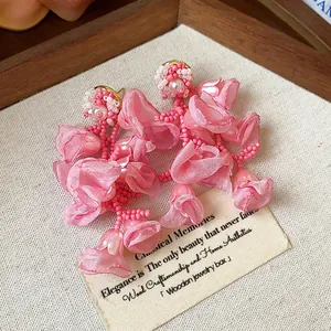 Close-up of pink chiffon flower earrings with pearl and bead details on a wooden tray