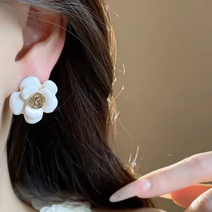 Gros plan élégant de boucles d'oreilles fleur en émail blanc avec rose dorée sur l'oreille