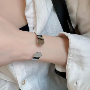 A close-up detail shot of an elegant minimalist irregular silver metal open bangle bracelet.