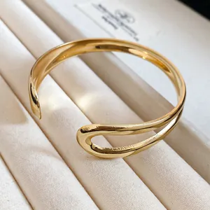 Macro view of a polished irregular gold cuff bracelet on a white jewelry display.