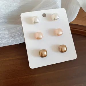 Close-up of three pairs of geometric square pearl stud earrings in elegant finishes