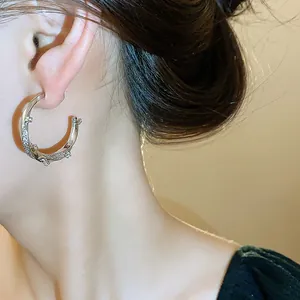 Close-up of zircon C-shaped earrings with 18k gold plating and silver pins on a model.
