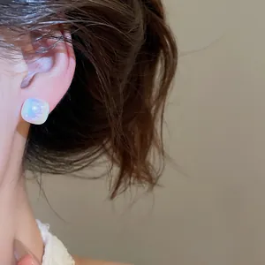 Close-up view of a geometric square stud earring with iridescent rainbow finish on ear