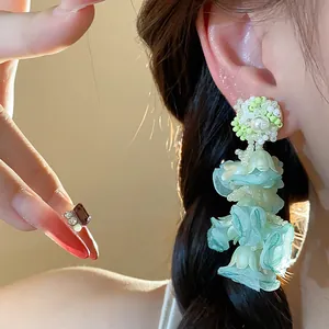 Detailed close-up of light green chiffon flower earrings with pearls and bead accents.
