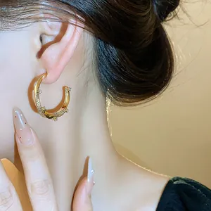 Macro view of an elegant 18k gold plated C-shaped earring with sparkling zircon on ear
