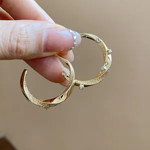 Detailed view of 18k gold plated C-shaped earrings with zircons and textured finish