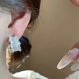 Detailaufnahme der plissierten silbernen C-förmigen Ohrstecker mit Zirkonia-Akzenten
