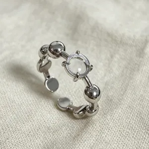 Primo piano di anello aperto in argento con zircone e dettagli a forma di sfera.