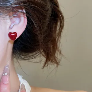 Close-up of a model wearing glossy red heart-shaped stud earrings for daily fashion.