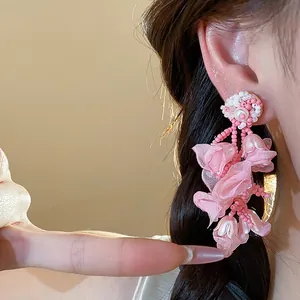 Detailed view of pink chiffon flower and pearl earrings with silver needle on model ear