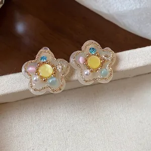 Pendientes de flor de resina con circonitas de colores y perlas sobre fondo de tela
