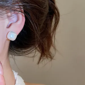 Detailed macro view of a elegant white iridescent square pearl stud earring on an ear