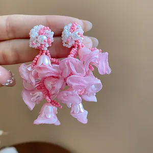 Close-up of pink chiffon flower earrings with beads and pearls on a silver needle.