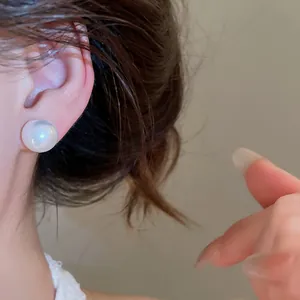 Close-up of elegant white pearl stud earring worn on model's ear showing high-end texture