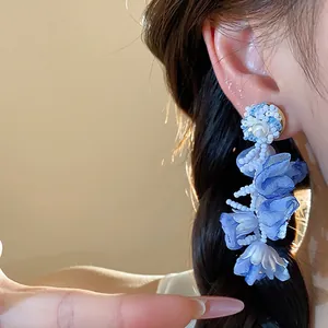 Close-up of blue chiffon flower earrings with pearl and bead detail worn by model