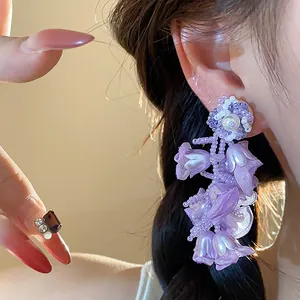 Close-up detail of elegant purple chiffon flower and pearl drop earrings worn on ear.