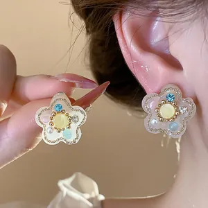 Primer plano de elegantes pendientes de flor de resina con perlas de colores y circonitas.