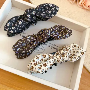 Detailed view of three floral pattern bow banana hair clips arranged in a white display tray