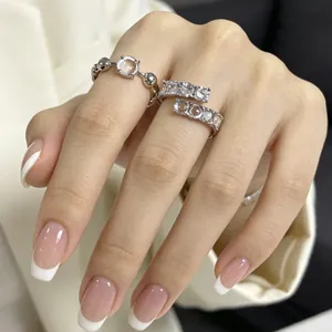 Primo piano di eleganti anelli in zircone e resina sulla mano con manicure bianca.
