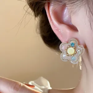 Vista detallada de pendientes de flor de resina con brillantes circonitas y perlas.