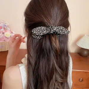 Rear view of a woman wearing a black floral print bow banana clip in wavy brown hair