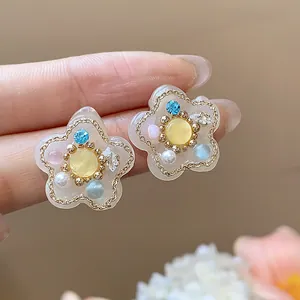 Primer plano de los pendientes de flores de resina con perlas y circonitas azules finas.