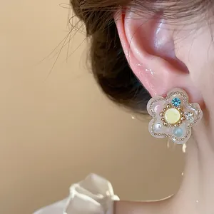 Primer plano de pendiente de flor de resina con cristales de colores y perlas en la oreja
