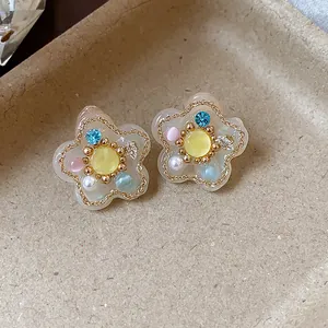 Detalle macro de pendientes de botón de flor de resina con perlas y gemas de colores
