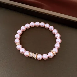Primo piano di un elegante bracciale di perle rosa con fiocco in zircone e finiture oro.