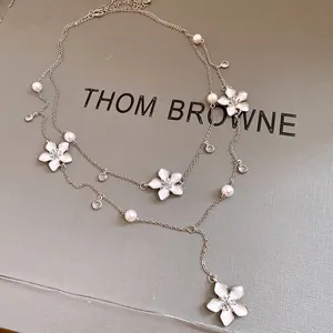 Vista dettagliata della collana a due strati con fiori in smalto bianco, perle e cristalli