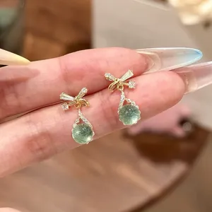 Close-up detail of elegant gold bow stud earrings with green round stones and zircon accents.