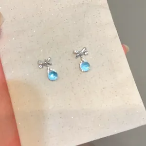 Elegant silver bowknot stud earrings featuring light blue teardrop zircon crystal dangles