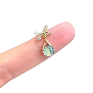 Elegant bowknot zircon earrings with green water drop pendant shown on finger