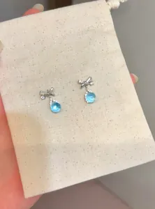 Detailed view of silver bow earrings with blue water-drop cubic zirconia stones