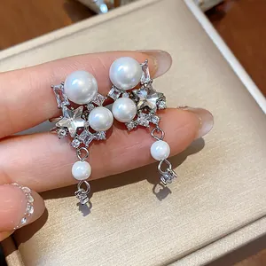 Close-up of elegant star zircon and pearl ear clips on a textured gold jewelry box