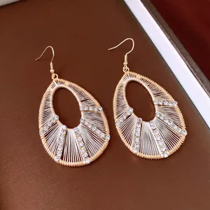 Detailed view of elegant gold teardrop earrings with white thread and sparkling rhinestones