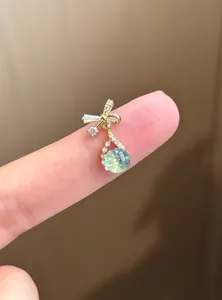 Close-up of elegant bow earrings with green zircon drop on finger display