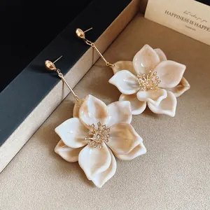 Primer plano de elegantes pendientes de flores de resina crema con brillantes strass.