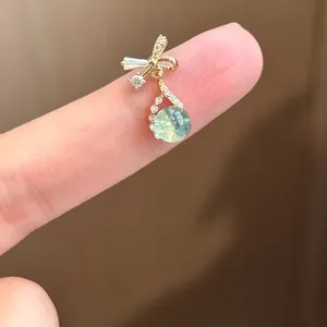 Exquisite gold bow stud earring with light green zircon drop shown on finger for scale